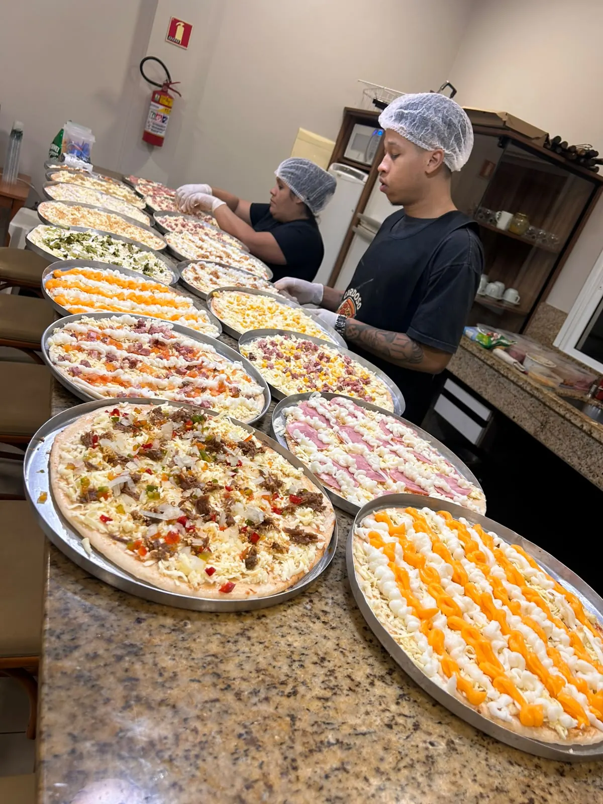 Equipe da Cardoso Pizza montando dezenas de pizzas no balcão de um evento